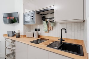 Una cocina moderna con un televisor de pantalla plana, una cafetera, un tostador, un lavabo y un organizador para cuchillos.
