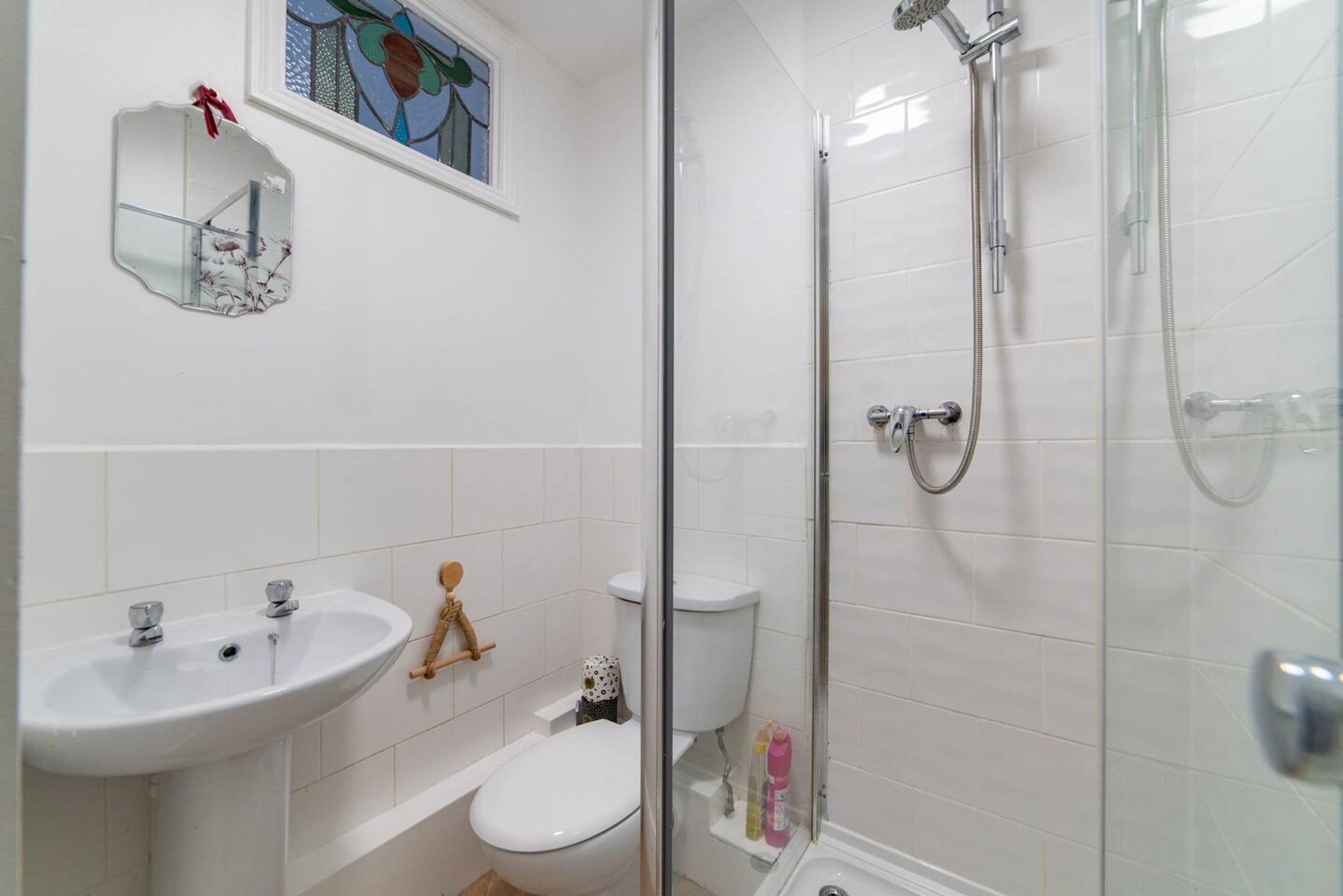 A bathroom with a sink, toilet, shower, and a mirror with a red ribbon.