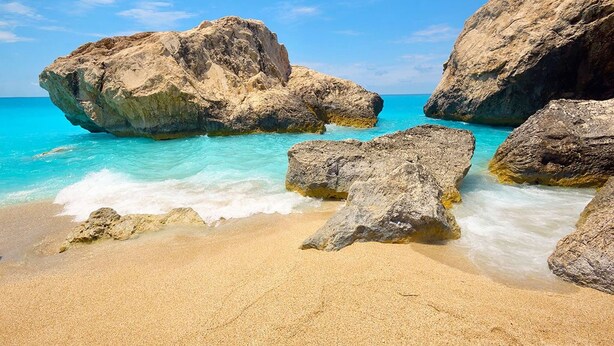 Een strand met grote rotsen en helder turquoise water.