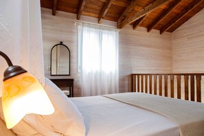 A wooden cabin room with a bed, a nightstand, a mirror, and a window with curtains.
