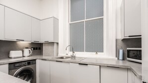 Cocina moderna con armarios blancos, lavadora integrada, un lavabo y una ventana con vistas decorativas.