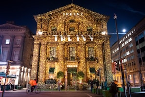 Ein historisches Gebäude mit der beleuchteten Aufschrift 'THE IVY', umgeben von städtischen Straßen und Fußgängern.