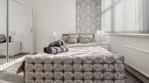 Un dormitorio moderno con una cama grande, una mesita de noche, una lámpara y una ventana con cortinas.