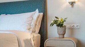 Een net opgemaakt bed met witte lakens, een nachtkastje met een plant erop en een wandlamp.