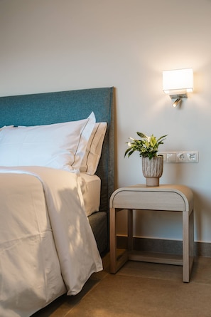 A neatly made bed with white linens, a bedside table with a plant, and a wall-mounted light fixture. - Kohyli Villas- Villa Two With Private Pool (Meganisi)
