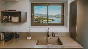 Een keuken met een ingebouwde spoelbak, een raam met uitzicht op een meer en bergen, en een plank met keukengerei.