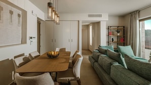 Een moderne woonkamer met een houten eettafel, beige banken en een boekenkast.