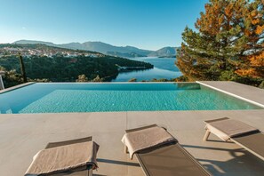 Ein Pool mit Liegestühlen und Handtüchern mit Blick auf einen See und Berge.