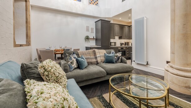 A spacious living area with a sofa, a glass coffee table, and a view of a kitchen and dining area. - Rare Historic Church Stained Glass Parking (Liverpool)
