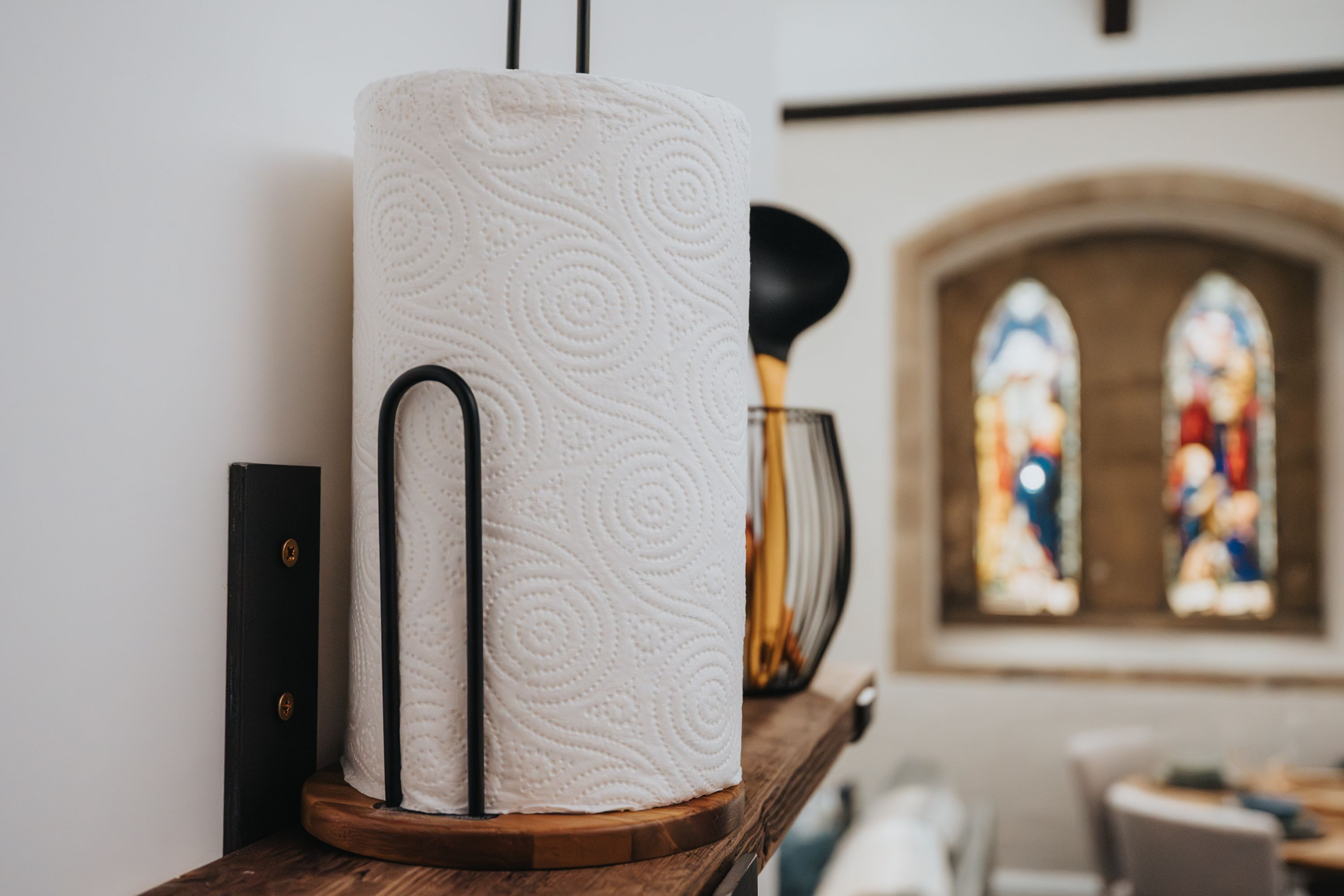 Un rollo de papel higiénico sobre un soporte de madera en una habitación con un ventanal de vitrales.