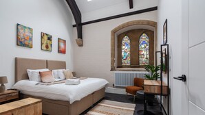 A bedroom with a bed, bedside table, and a window with stained glass. - Rare Historic Church Stained Glass Parking (Liverpool)