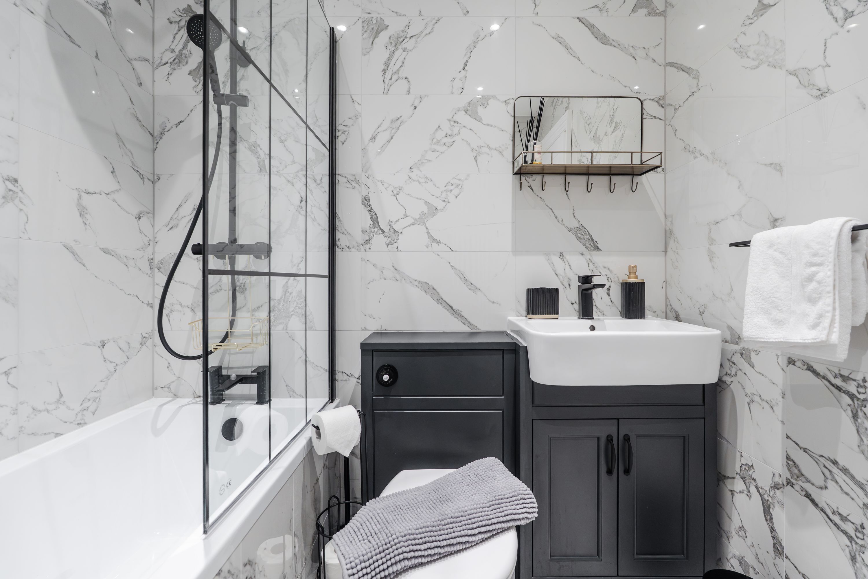 Een moderne badkamer met een douche met glazen wand, een witte wastafel en donkere kastjes.