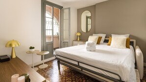 Une chambre à coucher avec un lit, des tables de chevet, un miroir et une vue sur l’extérieur, visible à travers une porte ouverte.