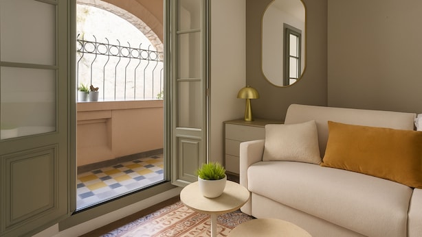 Une pièce avec un canapé, une petite table ronde ornée d’une plante, une lampe et un miroir au mur.