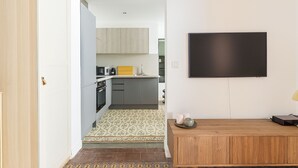 Une cuisine moderne avec des meubles gris, un pare-feu en carreaux et un téléviseur à écran plat fixé au mur.