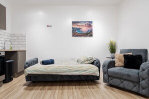 Un dormitorio moderno con una cama, un sofá gris, una mesita, una planta en maceta y un cuadro en la pared.