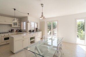 Une cuisine moderne avec une table à manger en verre, des meubles blancs et des luminaires suspendus.