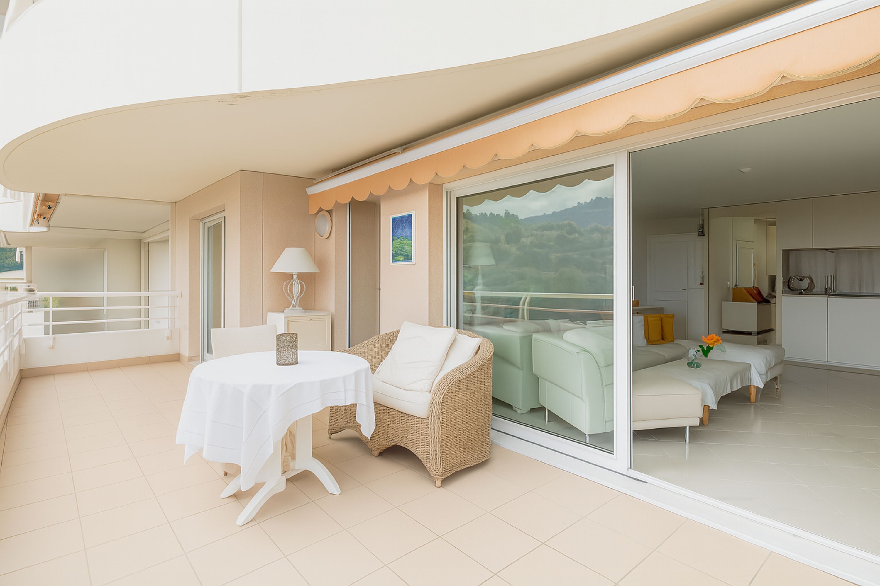 Un balcon avec une table et des chaises, un canapé et une porte-fenêtre coulissante donnant sur un espace intérieur comprenant un canapé et un coin cuisine.