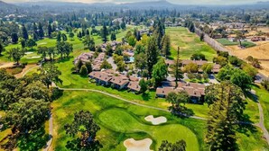 An aerial view of a golf course with residential buildings, a clear sky, and distant mountains. - Luxe Golf View Condo Prime Napa Location (Napa)