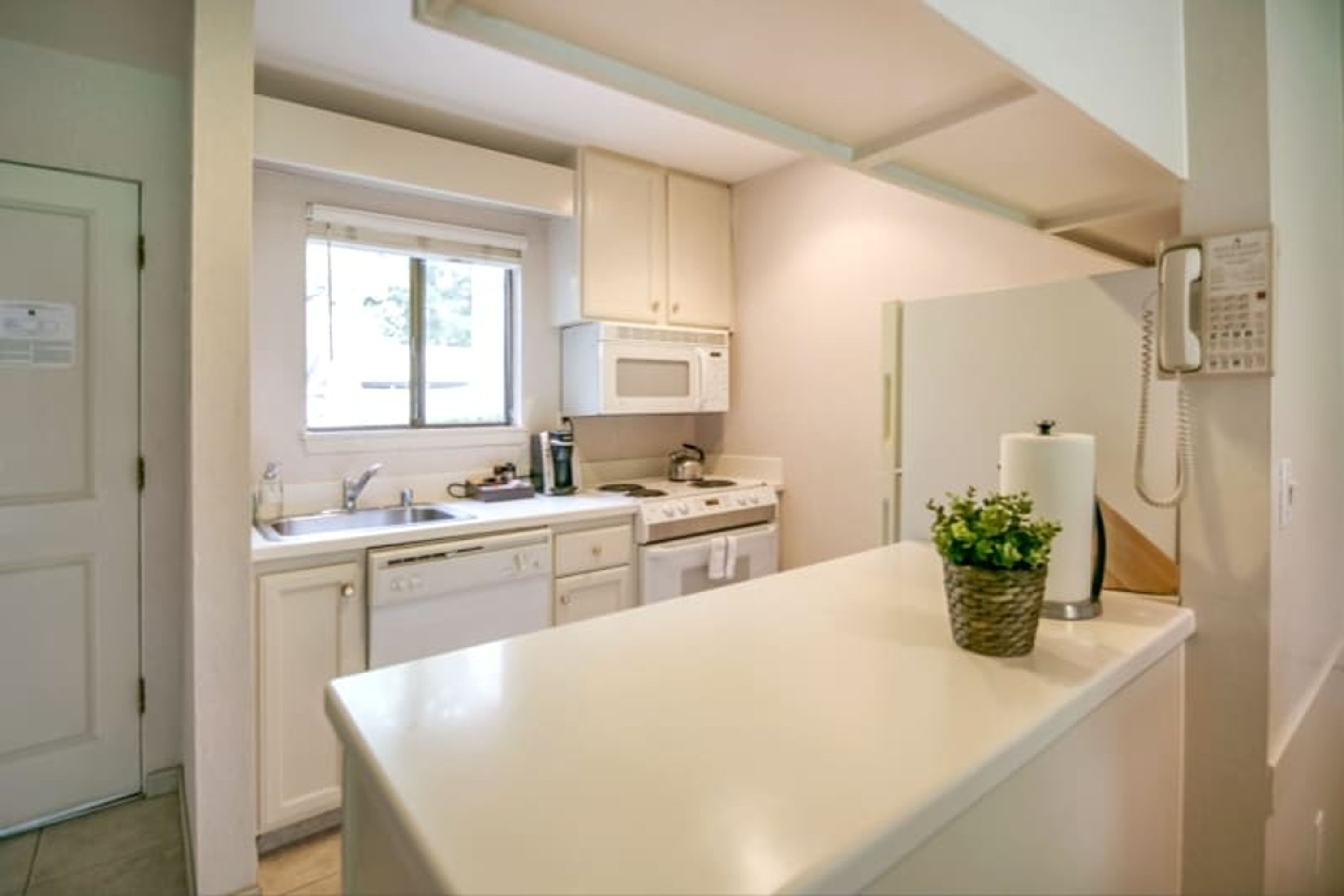 A kitchen with white cabinets, a microwave, a stove, a sink, and a telephone.