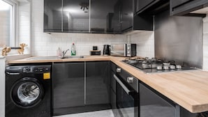 A compact kitchen with a dishwasher, stove, microwave, and black cabinets. - Next to LFC W M Desk Space City Links (Liverpool)