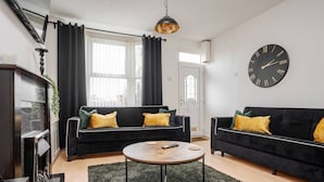 A modern living room with two black sofas, a round coffee table, a fireplace, and a large wall clock. - Next to LFC W M Desk Space City Links (Liverpool)