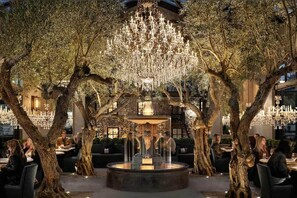 Un área de comedor al aire libre con árboles, una fuente y candelabros.