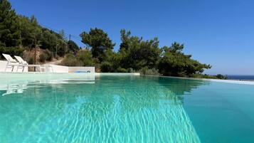 A clear blue infinity pool with lounge chairs and a view of the sea.