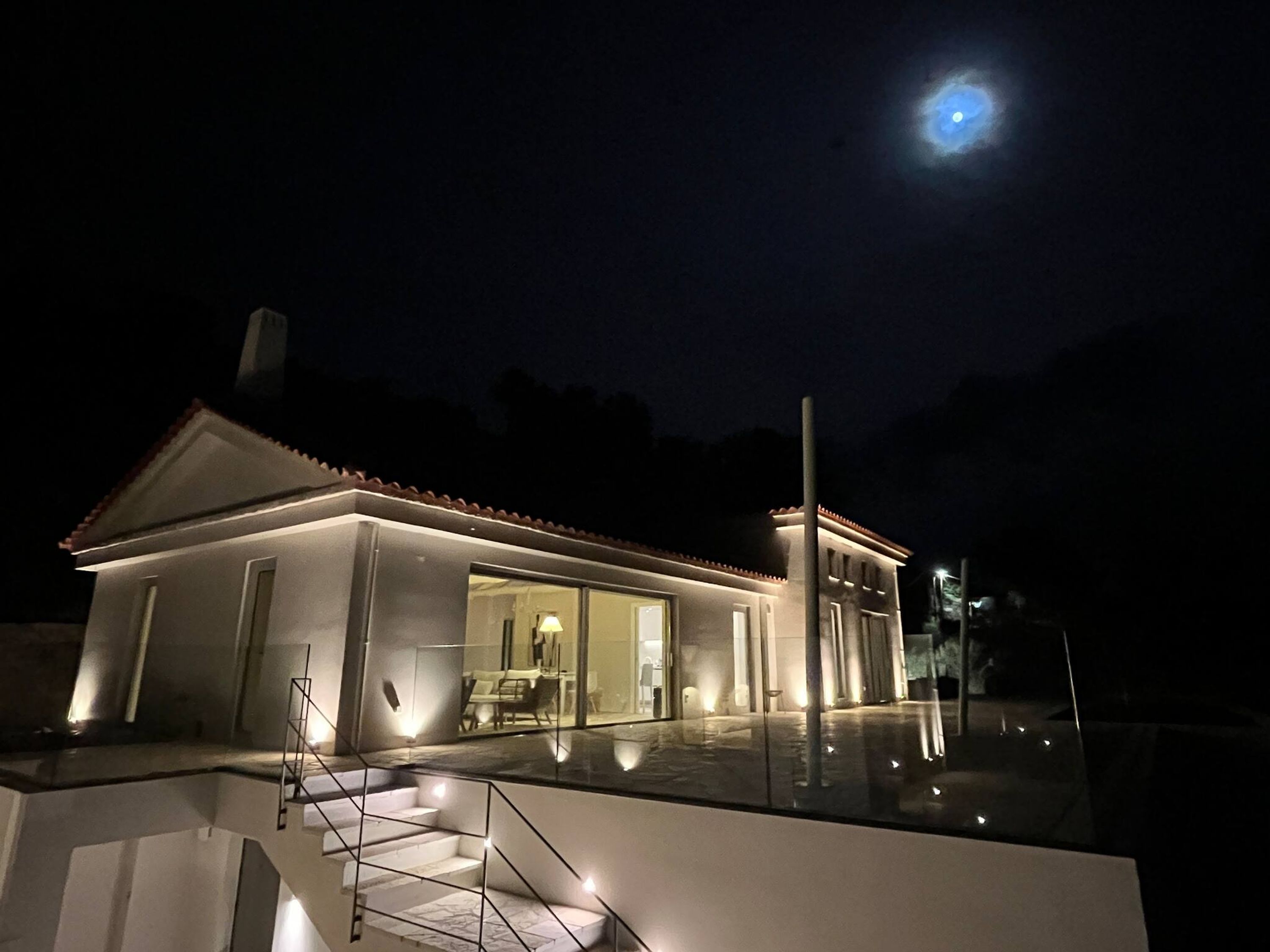 A modern house with a well-lit exterior and a visible staircase leading to the entrance.