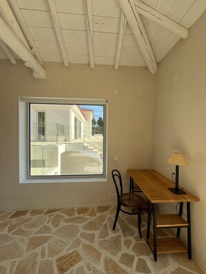 A room with a stone floor, a wooden table with a chair, a window, and a lamp. - Pasparo Estate in Samos (Samos)