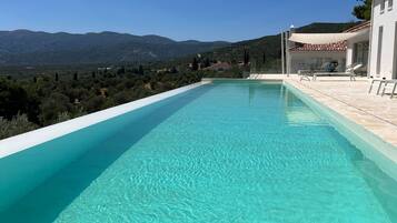 A clear swimming pool with a view of mountains and a white building with outdoor seating.