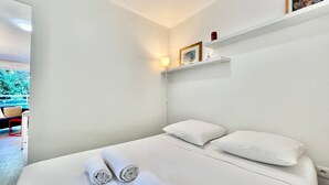 A hotel room with a bed, pillows, a bedside table, a lamp, and a shelf with decorative items. - Charming Studio at the Gates of Monte Carlo Per (Beausoleil)