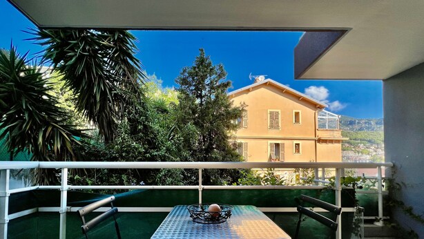 A balcony with a table and chairs, overlooking a building and greenery. - Charming Studio at the Gates of Monte Carlo Per (Beausoleil)