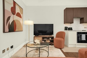 A modern living room with a flat-screen TV, a glass coffee table, a sofa, and a large abstract painting. - Brand new refurbished 2 bed flat in Kensington (London)