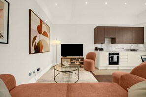 A modern living room with a sofa, a glass coffee table, a TV, and a lamp. - Brand new refurbished 2 bed flat in Kensington (London)