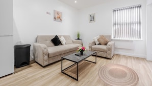 A modern living room with a sofa, a coffee table, a trash bin, and a window with blinds. - Great for Longer Stays W M Smart TV Parking (Liverpool)