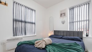 A bedroom with a bed, a radiator, a window with blinds, a wall-mounted mirror, and a picture. - Great for Longer Stays W M Smart TV Parking (Liverpool)