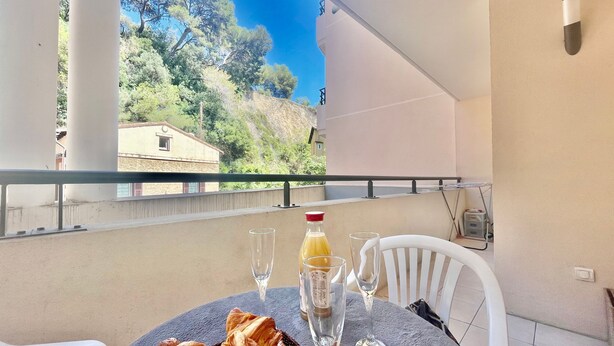 Een balkon met een tafel gedekt voor twee personen, met een mandje croissants, twee wijnglazen en een fles sinaasappelsap.