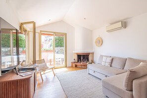 A modern living room with a sofa, a fireplace, a wooden table, and a glass door leading to an outdoor area. - Renovated House in the Center of Beausoleil (Beausoleil)