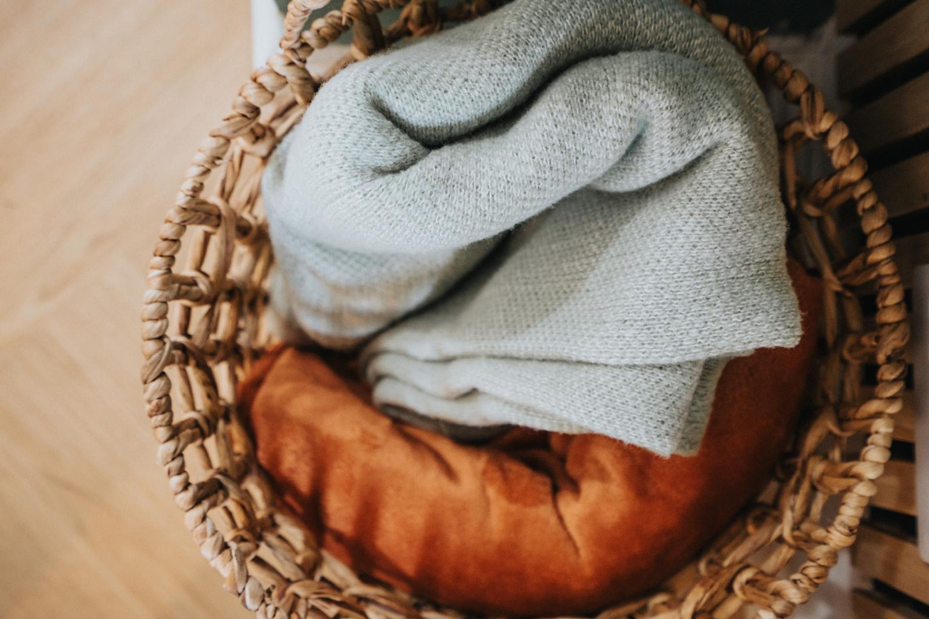 Una cesta tejida con un tejido gris doblado y un cojín marrón.