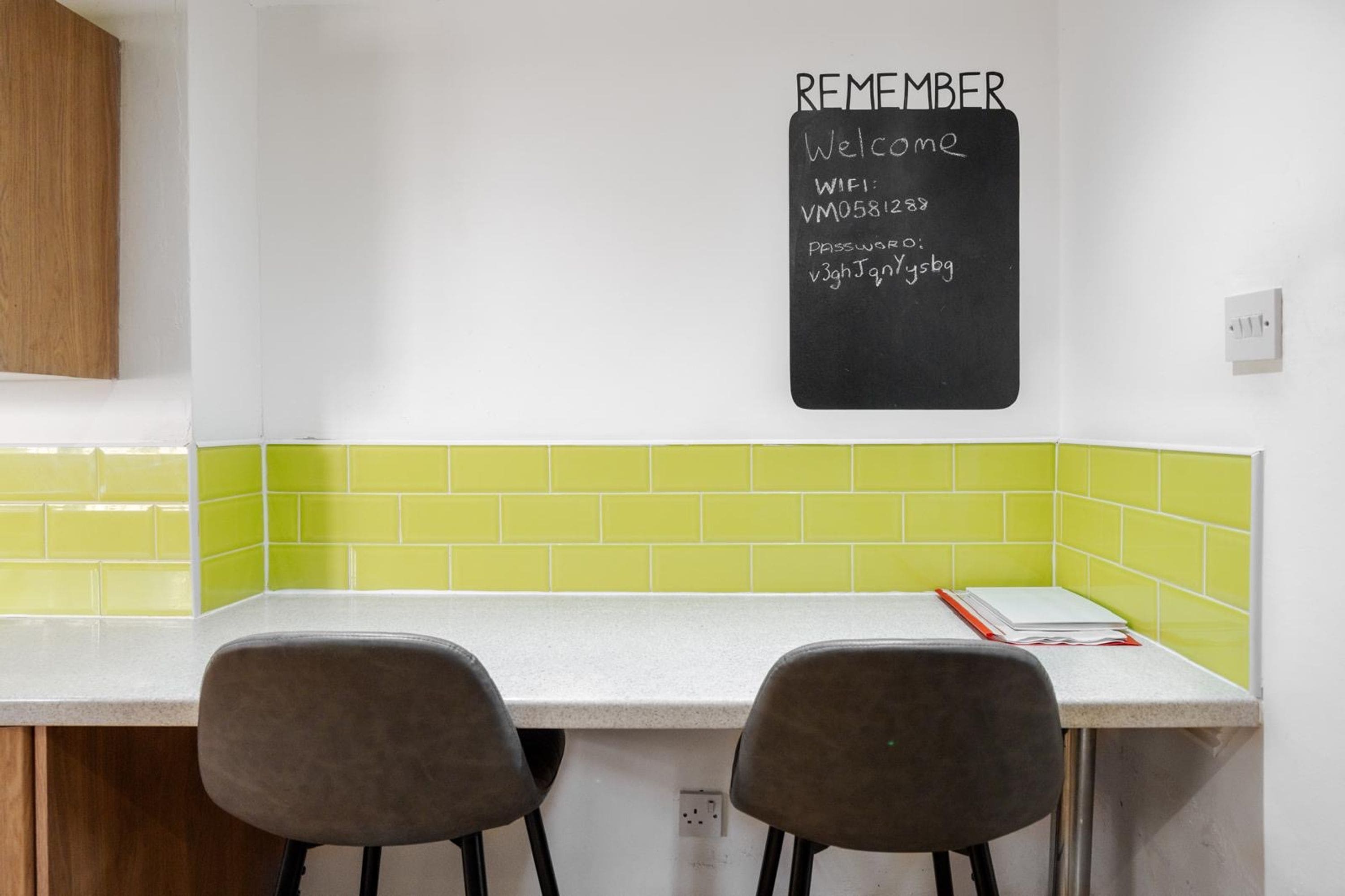 A kitchen with a chalkboard displaying WiFi and password details, two chairs, and a white countertop.