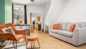 A modern living room with a sofa, armchair, and ottoman, a staircase, and a view into the kitchen. - 10 Mins to Crosby Beach Ensuite WC Parking (Liverpool)