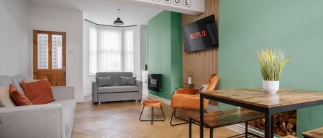 A modern living room with a sofa, armchair, coffee table, and a TV mounted on a green wall.