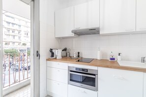 A modern kitchen with white cabinets, a wooden countertop, a built-in oven, and a view of a balcony with a cityscape. - Big Studio Biov s Central Menton Casino (Menton)