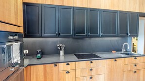 A modern kitchen with wooden cabinets, a black countertop, a built-in oven, and a sink. - Elegant Bel Epoque Apartment in Center of Menton (Menton)