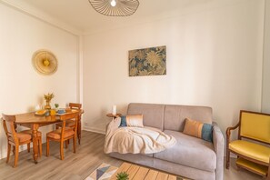 Ein Wohnzimmer mit einer Couch, einem Esstisch mit Stühlen, einem Couchtisch, einer Wandleuchte und einem gerahmten Kunstwerk.