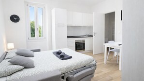 A modern bedroom with a bed, bedside table, and a view of a kitchen and bathroom. - Cozy Studio in the Heart of Menton Walk Everywhe (Menton)