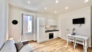 A modern apartment with a kitchenette, a dining area, a living room with a sofa, a TV mounted on the wall, and a window. - Cozy Studio in the Heart of Menton Walk Everywhe (Menton)