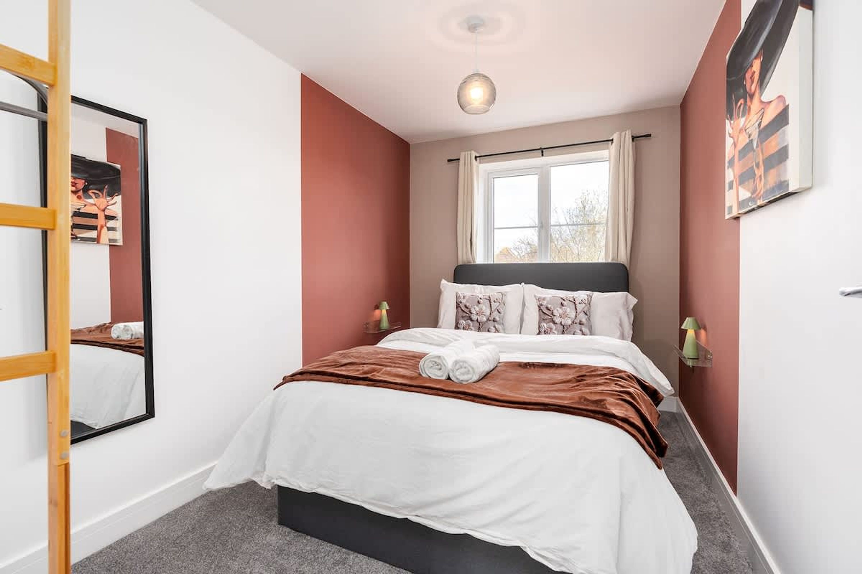 A bedroom with a bed, a window, a mirror, and artwork on the walls.