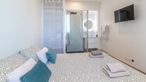 Una habitación de hotel moderna con cama, zona de ducha, televisor y baño.